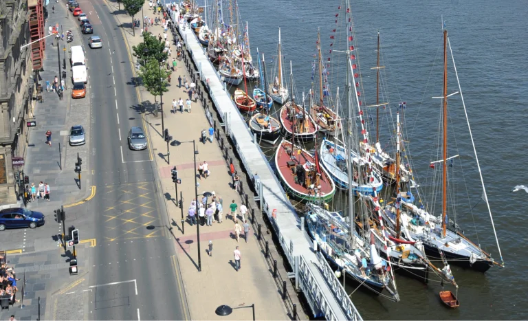 A aerial shot of Quayside with a row of boats parked on the side with people walking on the footpath 